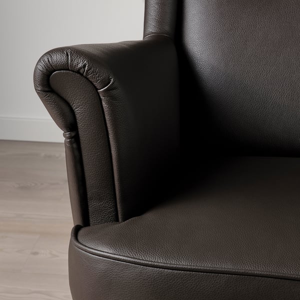 Dark brown leather wing chair, detailed armrest, smooth finish.