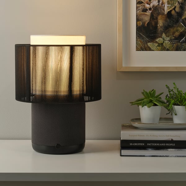 A modern table lamp with a built-in wifi speaker, emitting warm light.