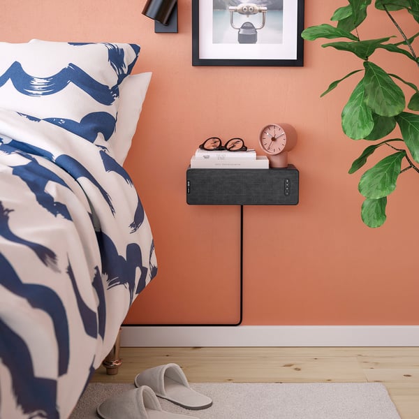 Bedroom setup with SYMFONISK speaker shelf in black. Colourful bedding, a clock, and green plant.