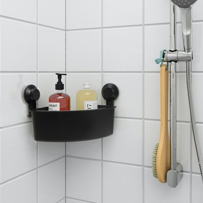 Black TISKEN corner shelf, suctioned to white bathroom tiles, holding shampoo bottles. Silver shower head nearby.