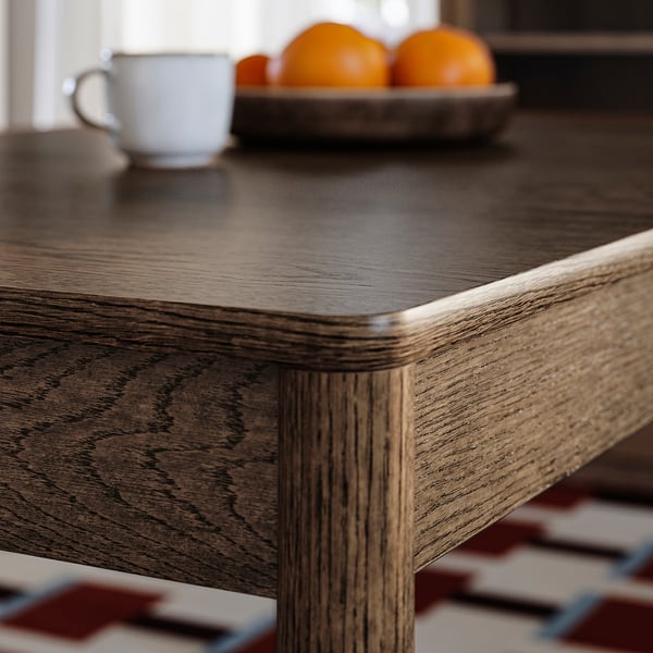 Wooden dining table close-up, sleek finish showcasing natural grain, set with coffee mug and oranges.