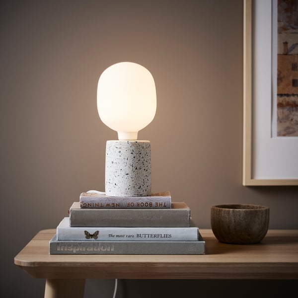 White table lamp on books, grey bowl on wooden table, framed picture.