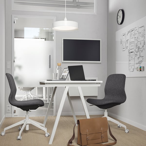 Minimalist office with TROTTEN desk, swivel chairs, laptop, tablet, leather bag, glass partition, tv, whiteboard, lamp, clock.