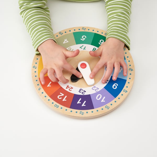 Childs hands adjusting wooden clock with color-coded hours and movable hands.