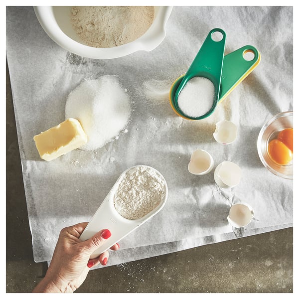 Hand holding measuring cup with flour among kitchen ingredients.