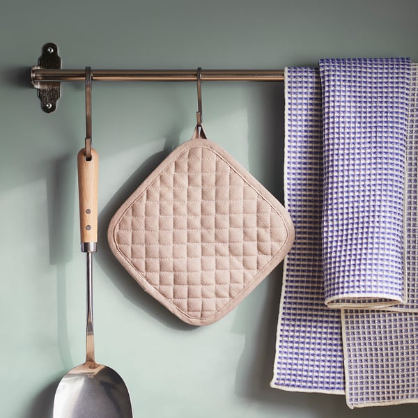Modern kitchen storage with beige diamond vålvårdad potholder, chequered towel, and metal ladle.