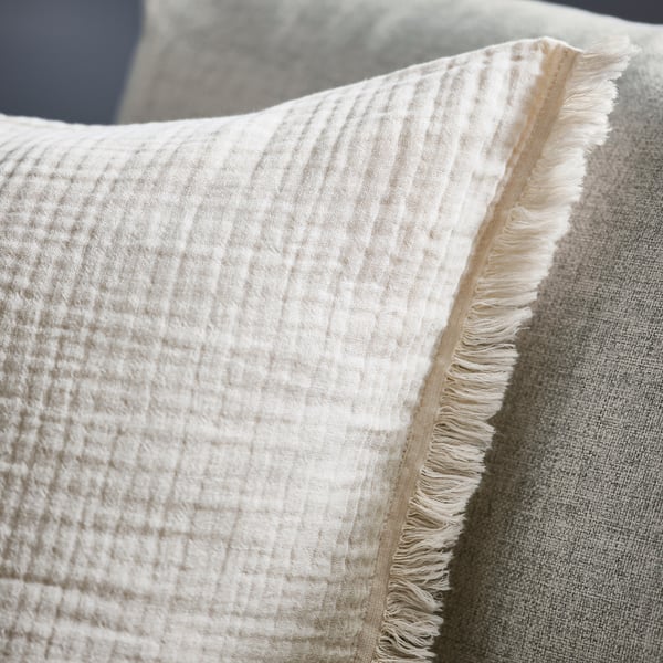 Close-up of soft, white, crinkled cotton cushion cover with raw, frayed edges.