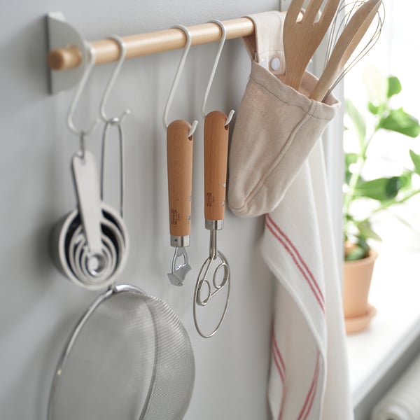 A kitchen organiser with hanging tools, including a danish dough whisk and measuring cups, efficiently stored for easy access.