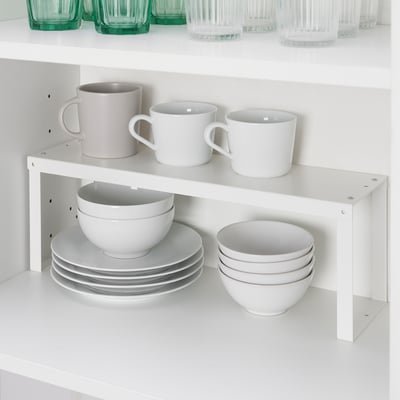 White shelf organiser stacks cups, bowls, and plates in cabinet for efficient storage.