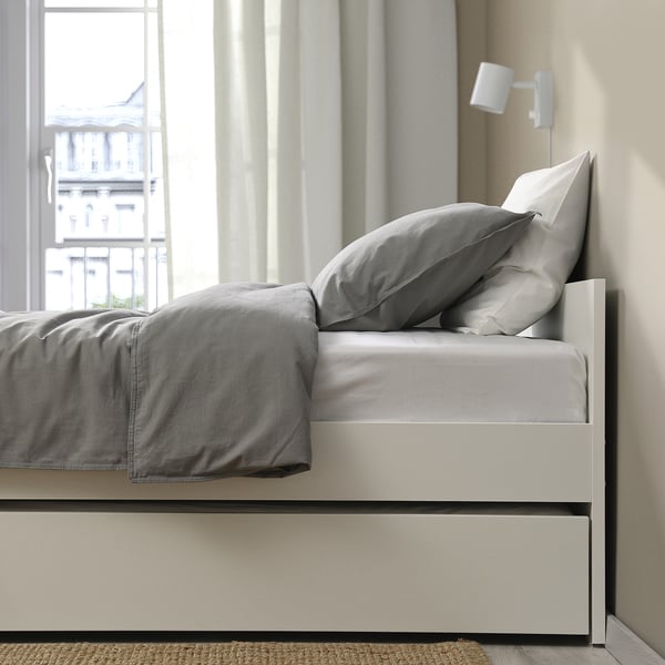 Modern bed frame with trundle, grey bedding, and wall-mounted light. Clean lines, versatile design for guest accommodation.