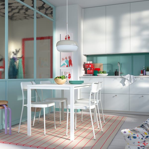 Bright kitchen with white VIHALS table and chairs. Large windows, blue accents, wooden bowls, and colourful rug.