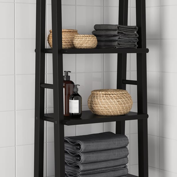Black wooden shelf unit with three levels. Holds folded grey towels and woven baskets against white tiled wall.