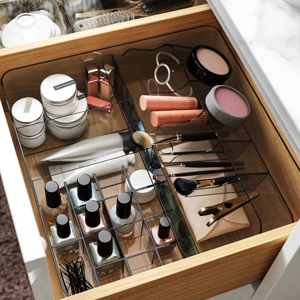 Clear plastic drawer organiser with multiple compartments for small items like makeup brushes, tubes, and containers.