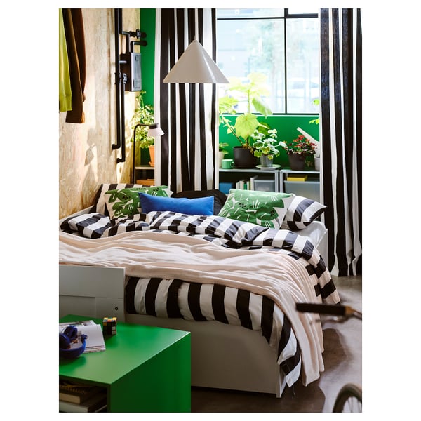 Bedroom with asymmetrical ZEBRASÄV recycled plastic pendant lamp over striped bed, surrounded by plants and green decor.
