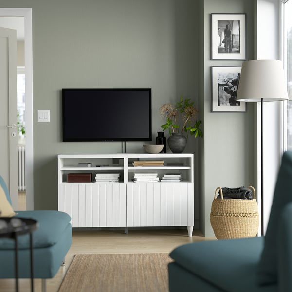 Modern living room with BESTÅ tv bench, flat screen tv, green wall, teal armchairs, and wooden floors.