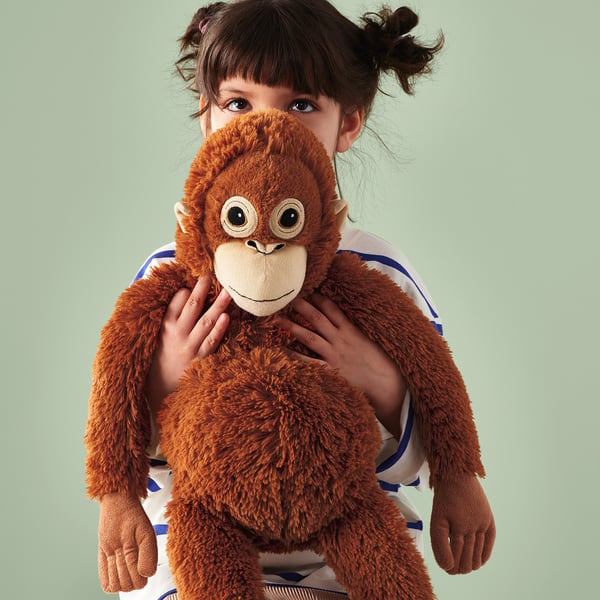 A child wearing a soft toy ape, which has a fastenings to hang around the waist or on a bag for hands-free carrying.