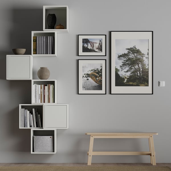 Modern room with grey walls, white modular shelves, and photos. Shelves hold books, a vase, and a basket. Wooden bench below.