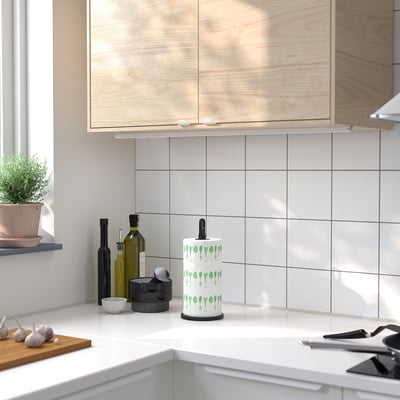 A kitchen counter with a white FAMILJ roll holder in green leaf design.