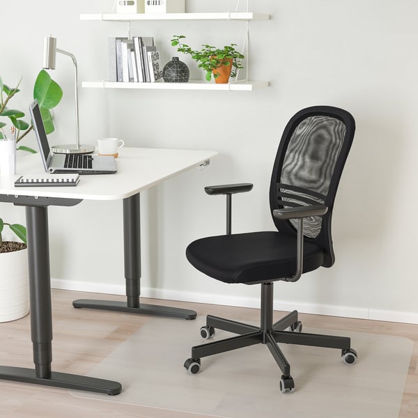 Ergonomic black office chair with mesh back, armrests, under compact desk with laptop and coffee.