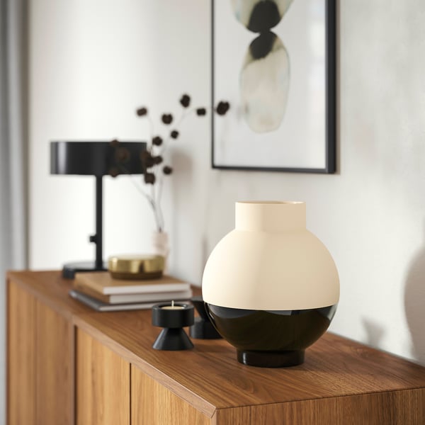 Elegant vase: beige top, black bottom, with candle, frame, and plant.