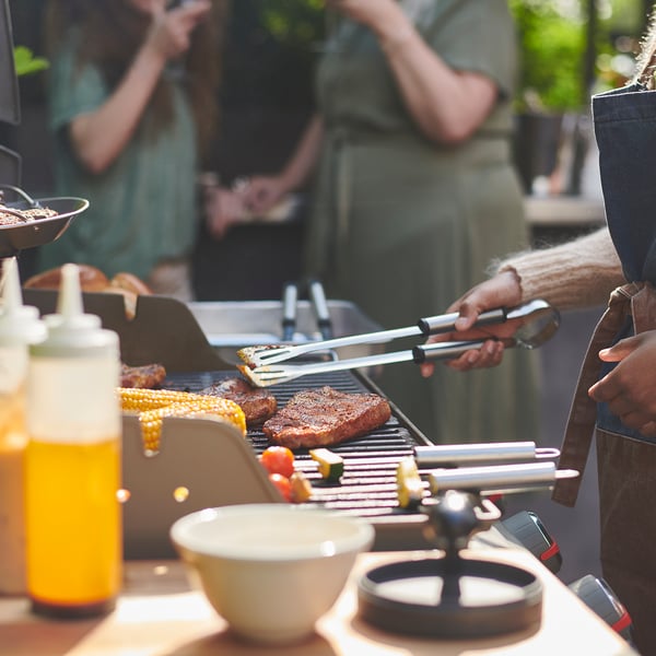 Barbecue scene with tools and food on grill.