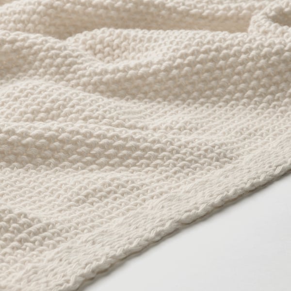 Close-up of soft, off-white knitted blanket, showcasing texture and craftsmanship.
