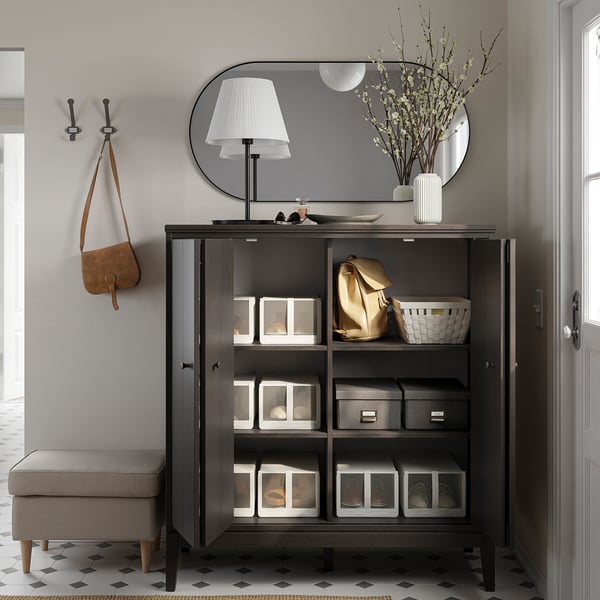 Modern entryway setup with IDANÄS black cabinet, mirror, lamp, and hooks. Includes organised storage with clear boxes and a bench.
