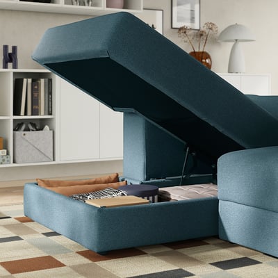 Modular sofa with open storage compartment, revealing cushions, books, and a blanket under raised seat.
