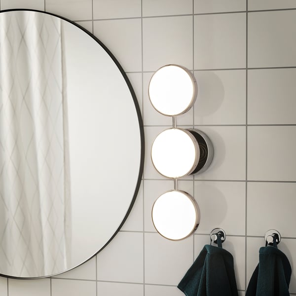 Large round mirror in bathroom, flanked by triple light fixture. Dark towels hang below.