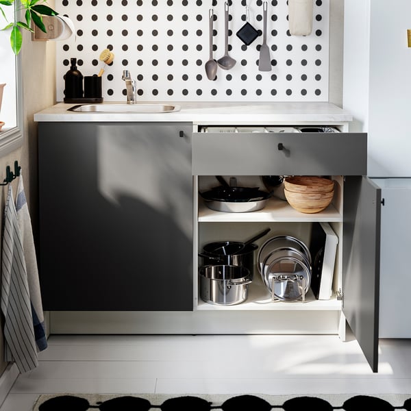 Modern kitchen with open drawer showing pots, pans, and utensils on polka dot wall.