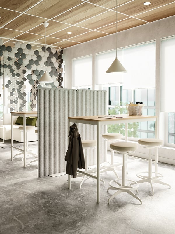 Modern office with LIDKULLEN sit-stand chairs, high table, wooden/metal elements, lights, large windows, grey carpet.