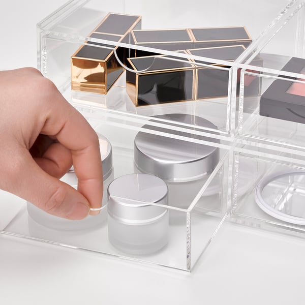 Hand reaching into clear, stackable acrylic storage drawers organising makeup and jewellery.