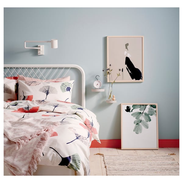 Modern bedroom with white metal bed, floral bedding, art prints, and wall sconce.
