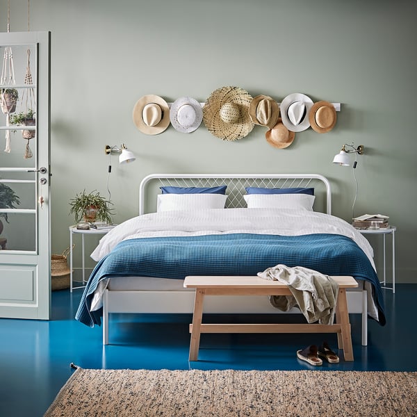 Modern bedroom with white metal bed, blue linens, wall-mounted hats, white walls, and blue floor.