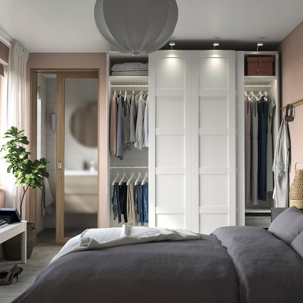 Modern bedroom with PAX wardrobe in white, sliding doors, grey bedding, hanging clothes, and a grey pendant light above the bed.