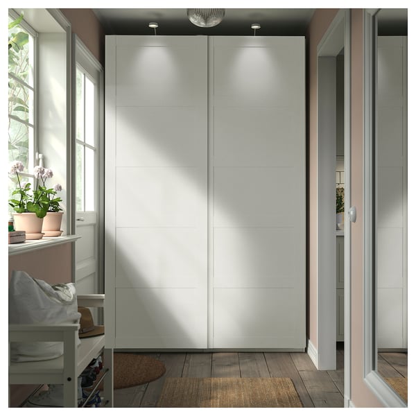 A white PAX wardrobe with sliding doors in a modern room, featuring minimalist design and integrated lighting.