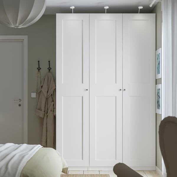 Tall, narrow white PAX wardrobe against sage green wall, with sleek knobs & grey door nearby. Dwarfs other items, showing large capacity.