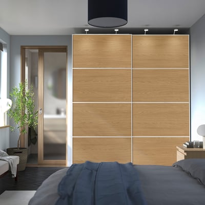 Modern bedroom with large oak PAX wardrobe. Neutral decor, blue bed, glass bathroom door.
