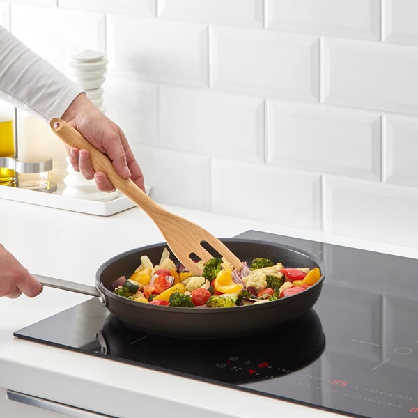 Person stirring colourful veggies in non-stick pan on induction cooktop.