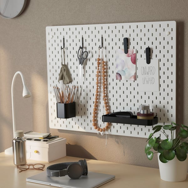 A wall-mounted pegboard organiser displays items like scissors, headphones, and a plant with notes, demonstrating efficient storage and accessibility.