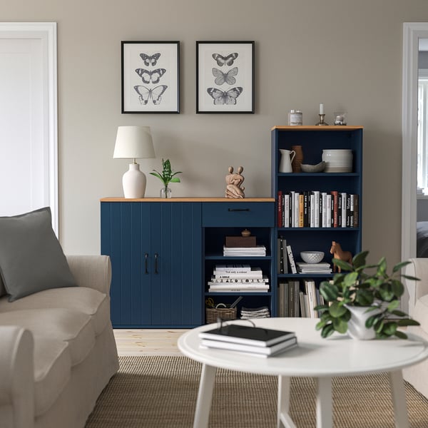Modern living room with beige sofa, blue SKRUVBY furniture, books, decor, butterfly prints, and a green plant.