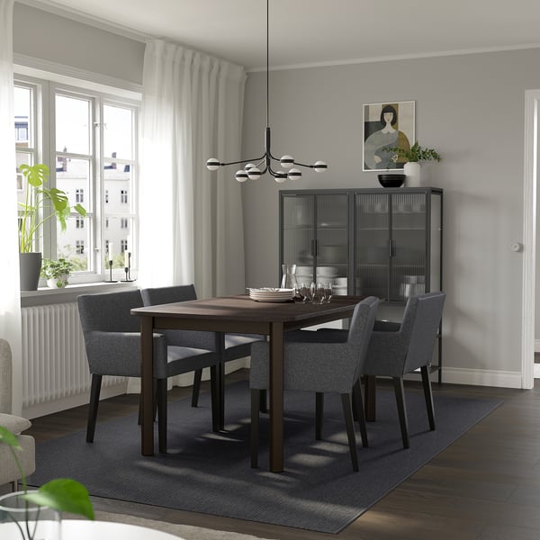Modern dining room with dark wood STRANDTORP table, 4 grey chairs, glass cabinet, and minimalist decor.