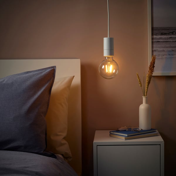 Cosy bedroom with SUNNEBY pendant lamp, warm light, bedside table, book, dried flowers, grey pillow, blue blanket.