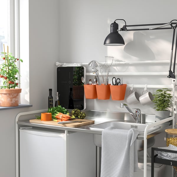 Modern kitchen with white sink, black lamp, orange containers, plants, grey towel.