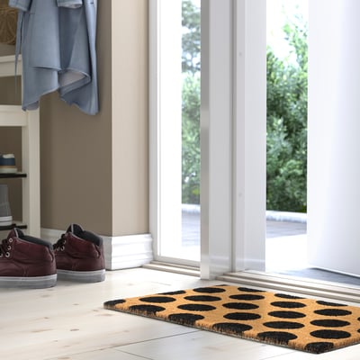TÅGFORDON doormat, rectangular, tan with black dots, near trainers, in front of a bright window.