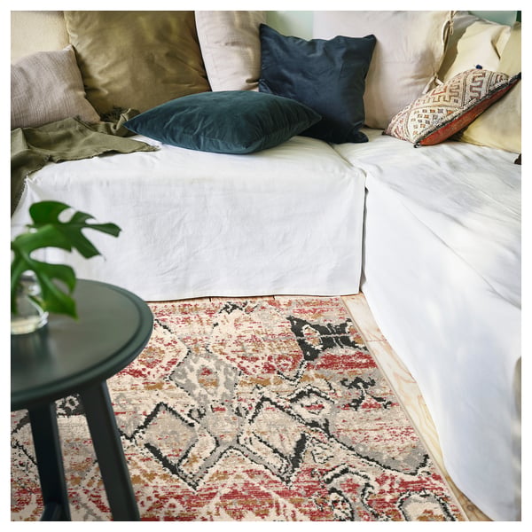Comfortable bed with colourful pillows, green plant on black table, red and beige patterned rug.