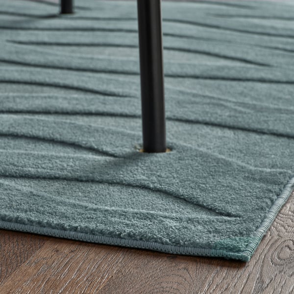 A blue, 3d-patterned rug on a wooden floor with a black pole in the centre. The rug has a low pile and an anti-slip backing.