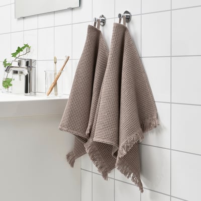 VALLASÅN towels hang on wall, beige-brown, waffle texture, fringed ends.