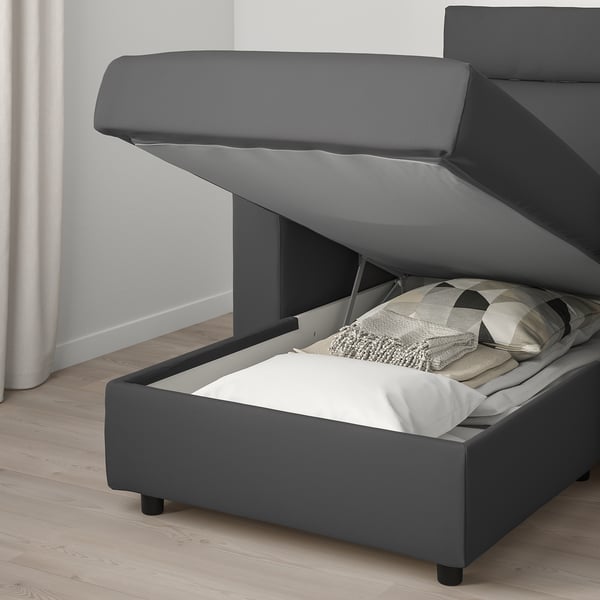 Modern grey sofa bed with open storage underneath, revealing folded blankets and pillows. Yelling comfort and functionality.