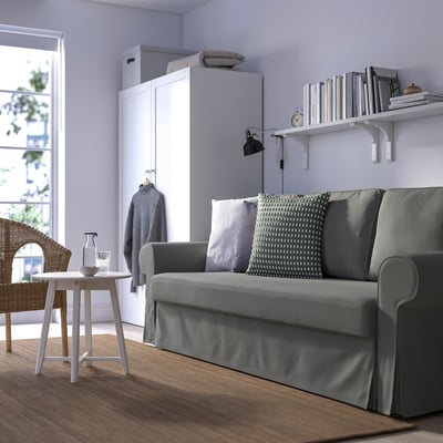 Grey sofa-bed near bookshelf, bright room